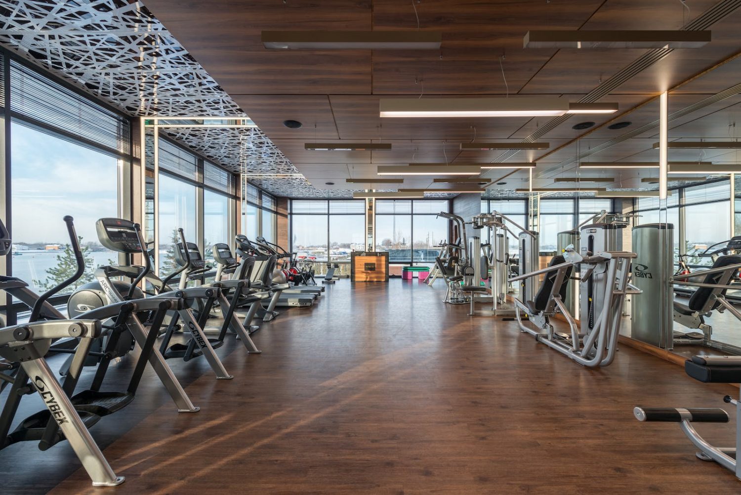 Interior of modern spacious fitness club with various sports machines and equipment placed on parquet floor near panoramic windows